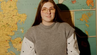 Emilie Lykke Nielsen foran et landkort og ved et kateder med en bunke bøger.