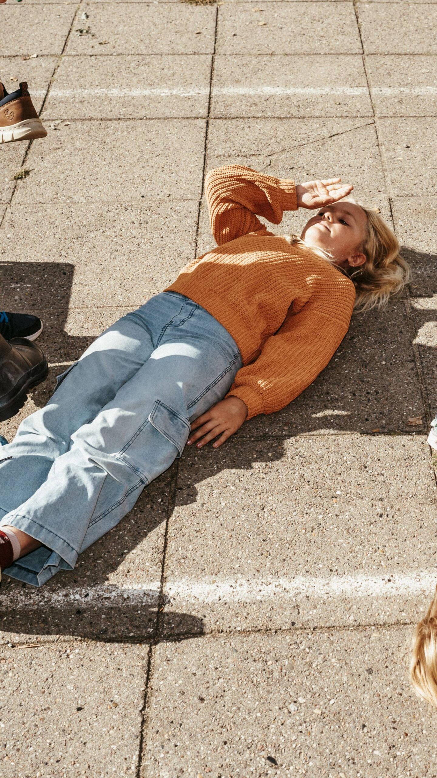 Pige ligger på ryggen i skolegården, hvor man laver øvelse med sko og støvler.