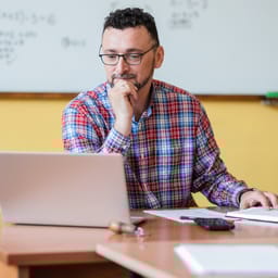 Mandlig lærer ved kateder kigger på sin bærbare pc