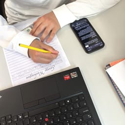 Billede af en elev der sidder og skriver i hånden med sin telefon ved siden af