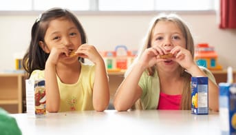 To små piger spiser mad i et klasselokale