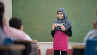 Pige med tørklæde holder oplæg for klassen foran tavlen