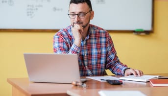 Mandlig lærer ved kateder kigger på sin bærbare pc