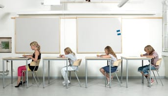 Fire elever ved skoleborde på række