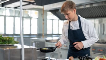 Dreng i gang med stegepanden i skolekøkken