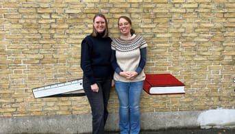 Maria Bruun-Jensen og Maria Sanko står lænet op ad en gul murstensvæg.