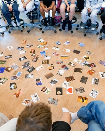 En gruppe af elever sidder i en rundkreds med billeder lagt rundt på gulvet