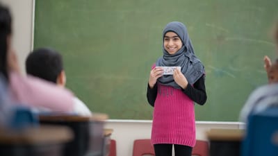 Pige med tørklæde holder oplæg for klassen foran tavlen