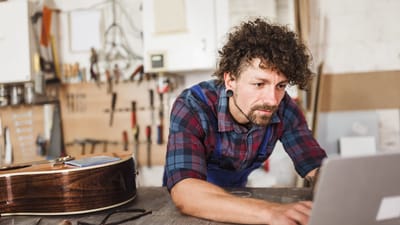 Ung mand reparerer guitar i værksted