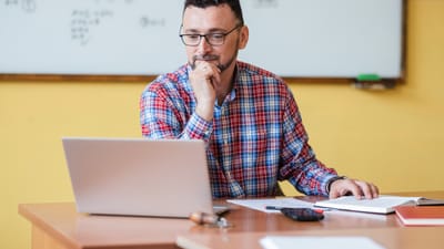Mandlig lærer ved kateder kigger på sin bærbare pc