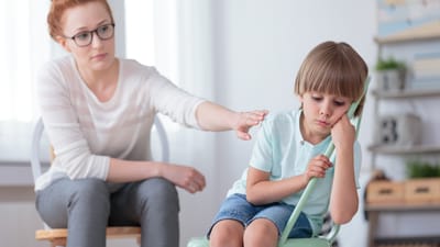 Lærer lægger en arm på skulderen af lille trist dreng, der vender hovedet væk