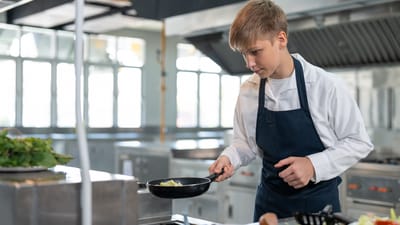 Dreng i gang med stegepanden i skolekøkken