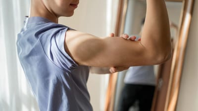 Teenagedreng mærker på sin biceps foran spejlet
