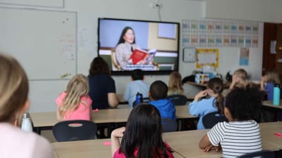 Elever kigger på tv-skærm, hvor en kvinde læser højt