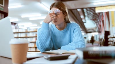 Kvinde gnider øjnene af træthed, mens hun studerer på et bibliotek