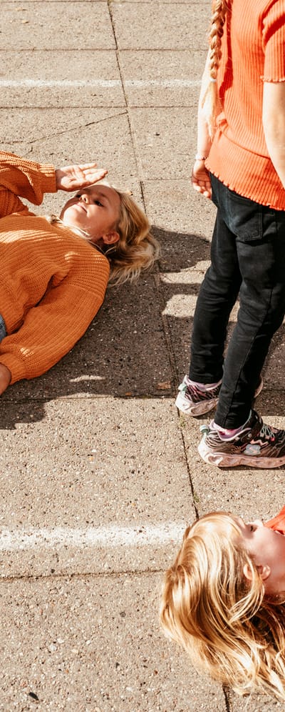 Pige ligger på ryggen i skolegården, hvor man laver øvelse med sko og støvler.