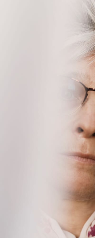 Portræt af Lone, der står mellem lyse gardiner